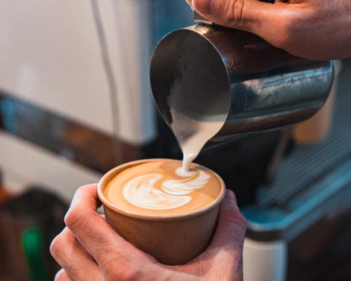 A barista pours a beautiful latte with art foam on top.