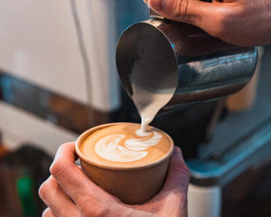 A barista pours a beautiful latte with art foam on top.